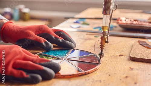Artisan Crafting Colorful Stained Glass Mosaic with a Soldering Iron and Protective Gloves in a Workshop