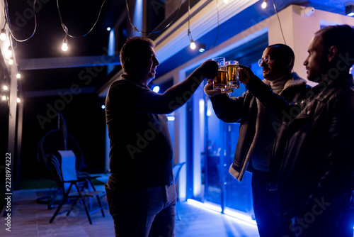 Obraz na plátně Friends enjoying a casual gathering outdoors with beer and festive lighting duri