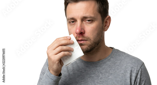 A single adult man experiencing a runny nose and nasal congestion, holding a folded tissue near his nose, slightly reddened nostrils and a tired expression