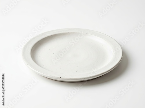 A single, minimalist, off-white ceramic dinner plate with a subtle speckled texture, presented at a high angle on a clean, solid white background.
