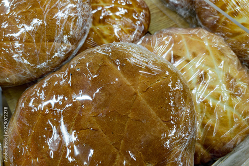 Multiple round loaves of bread wrapped tightly in clear plastic wrap, showcasing a golden-brown crust. The bread appears soft and freshly baked, arranged closely together on a wooden or rustic surface