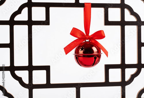 Red christmas jingle bell hanging with silk bow on traditional dark wood chinese lattice frame over white background