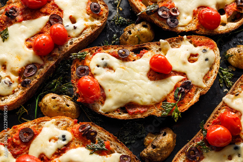 Halloween bruschetta toasts with ghost shaped melted cheese, cherry tomatoes, black olives and spooky mushrooms, close-up