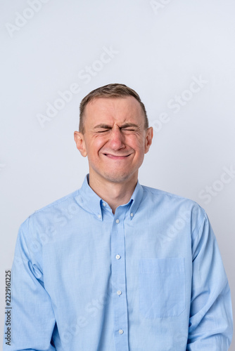 Obraz na plátně Man in a light blue shirt grimacing strongly, squeezing eyes shut and wrinkling