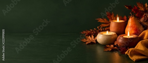 Thanksgiving autumn still life with pumpkins, candles and fall leaves on dark green background