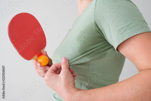 The woman has a wet sweat stain on her T‑shirt. A person is exercising and has become sweaty.