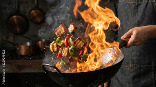 Professional chef tossing meat and vegetables in a wok with dramatic high flames.