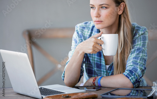 Thoughtful Young Woman Holding Coffee Cup Beside Laptop