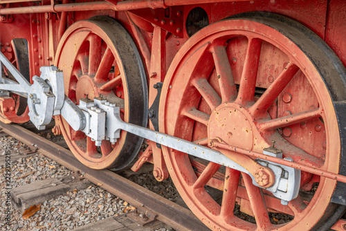 Close-up of red driving wheels and white connecting rods on a historic steam locomotive. Weathered metal, rusty details and vintage railway engineering