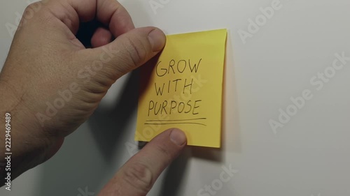 GROW WITH PURPOSE on a Yellow Sticky Note Held Against a Wall