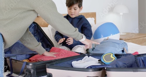 Parent and child packing suitcases on bed near backpack, preparing for trip, child handing sweater