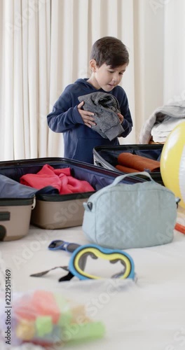 Vertical video: Asian mother and youth son packing clothes into open suitcases on bed for trip