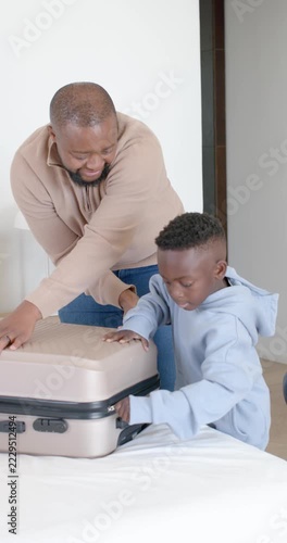 Vertical video: African American father teaching teenage sons to open stuck luggage zipper on bed