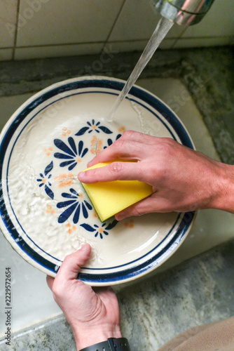 Hands washing a decorative plate under running water at the kitchen sink