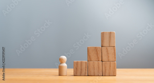 Wooden figure standing in front of wooden block staircases representing career growth, success, and business goal achievement