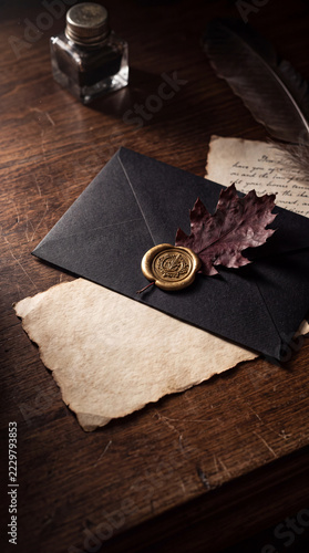 black envelope with a gold wax seal, dried dark burgundy oak leaf tucked into the seal, antique parchment card with blank writing space, resting on a dark walnut table, romantic gothic autumn 