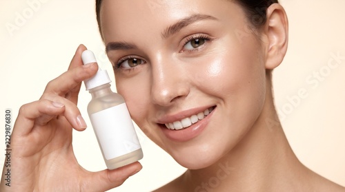 Close up portrait of a smiling woman holding a blank serum dropper bottle mockup