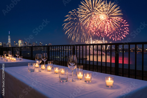 Candlelit rooftop dinner table with city fireworks at night