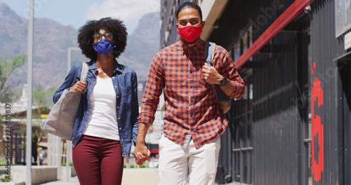 Diverse couple wearing face masks walking and holding hands