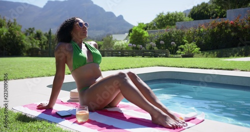 Vertical video: Woman in bikini tapping phone showing travel icons over pool, glass, planning trip