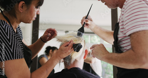 Focused diverse male and female hairdressers dying hair of female client at salon