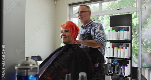 Focused caucasian male hairdresser styling pink hair of happy female client at salon, copy space