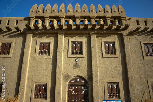 Facade of a traditional mud building with decorated wooden windows and spiky parapet, Mopti Region, Djenne, Mali