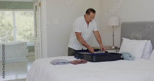 Senior man packing suitcase on bed in bright, cozy bedroom, at home