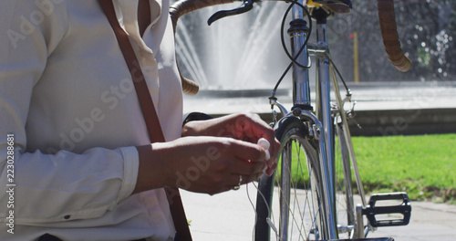 African american woman with bike putting earphones on in city park