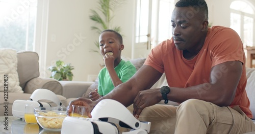 Reaching father in orange T-shirt grabbing VR headset on coffee table at home, copy space
