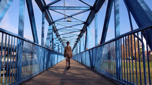 Girl in a long sweater goes on a metal bridge.