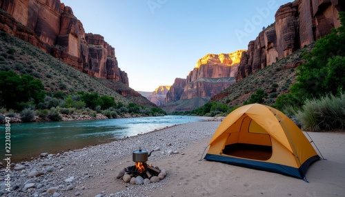 Scenic wilderness campsite with yellow tent and campfire by a river in a red rock canyon at golden hour