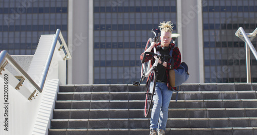 Thoughtful albino african american man with dreadlocks going down stairs with bike