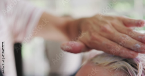 Close up of hand of caucasian male hairdresser dying hair of client at salon, copy space