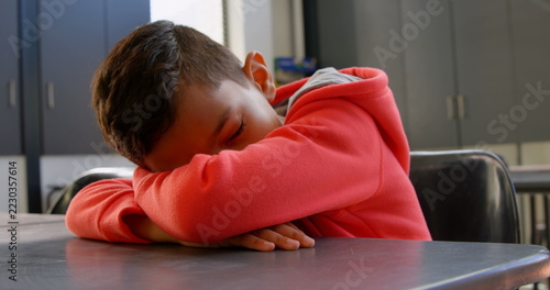 Front view of Asian schoolboy sleeping over the desk in classroom at school