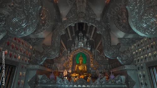 golden buddha statue inside ornate Silver Temple interior, sunlight illuminating intricate carved metal architecture of traditional Thai shrine Wat Sri Suphan 4k