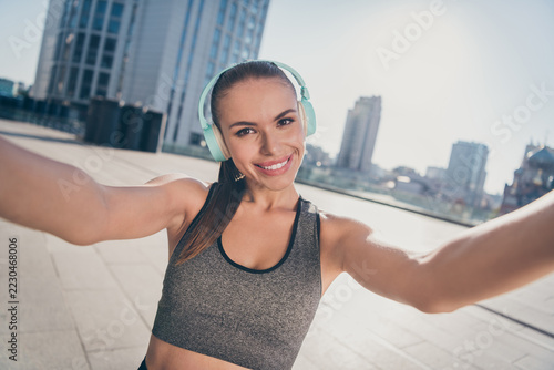 Portrait of sportive energetic strong lady listen audio headset early regime training make selfie outside