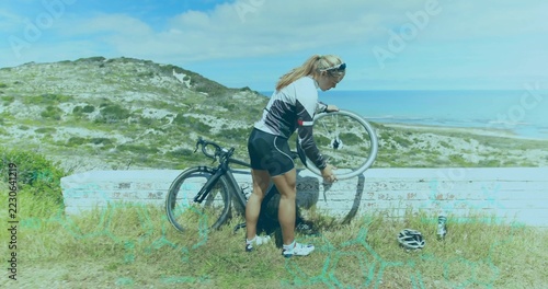 Holding front wheel, cyclist wearing cycling jersey, fixing road bike at coast with helmet bottle