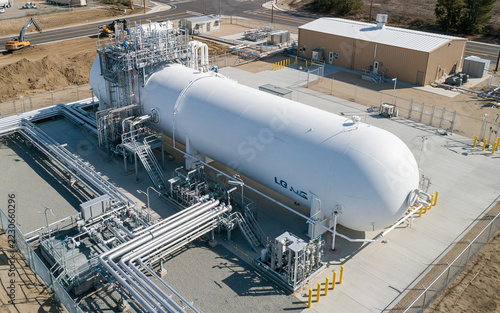 Aerial view of an LNG gas tank facility featuring a large white cylindrical tank and industrial equipment within a fenced enclosure