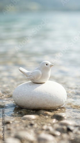 Small white ceramic bird figurine perched on a smooth white stone by the water.