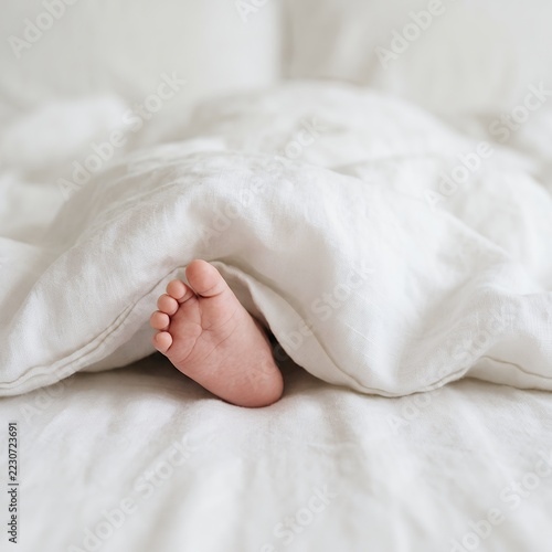 Tiny baby foot peeking out from under a white duvet on a bed.