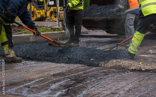 Team of construction workers spreading and leveling hot asphalt mixture on a damaged road surface during asphalt patching repairs.