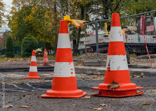 Orange traffic cones with fallen autumn leaves standing on a street repair site in a residential yard.