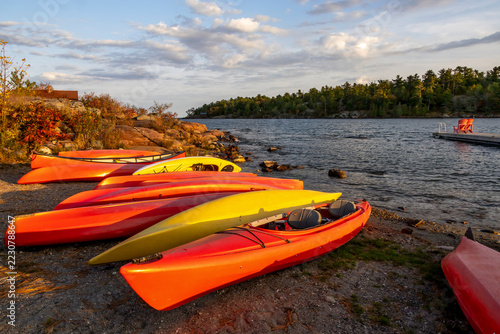 Vibrant kayaks line the shore of Killarney Channel, Ontario at sunset, creating a picturesque scene with calm waters and lush greenery.