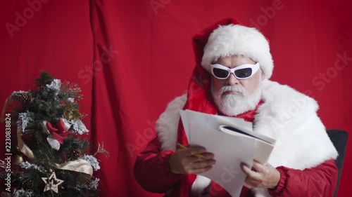 Modern Santa reviews Christmas letters and discards one beside small tree