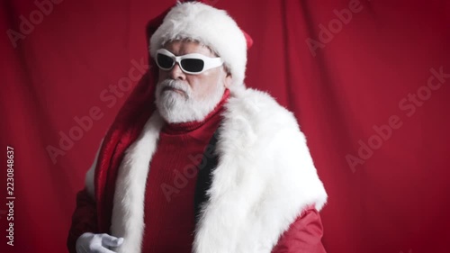 Cool Santa removes white sunglasses and walks out against red background