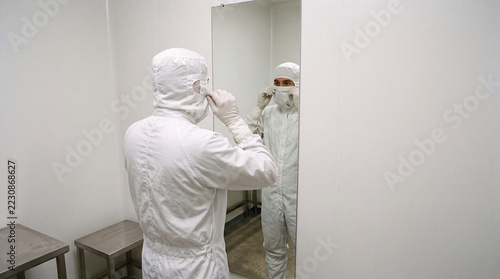 Operator adjusting hood at mirror in cleanroom gowning airlock people staff industry hygiene