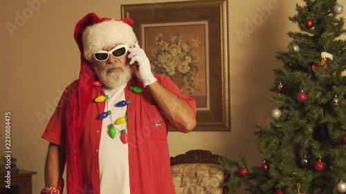 Modern Santa talks on smartphone and checks watch beside Christmas tree
