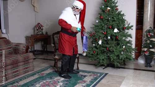 Modern Santa carries blue gift box and places it by Christmas tree