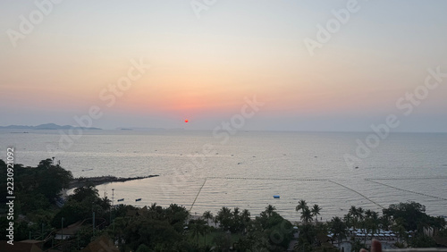 Fotografie Hazy pink sunset over the calm sea seen from above a palm-lined coast, Pattaya,